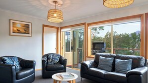 Ein modernes Wohnzimmer mit Ledersofas, einem runden Holztisch und großen Fenstern mit Blick ins Freie.