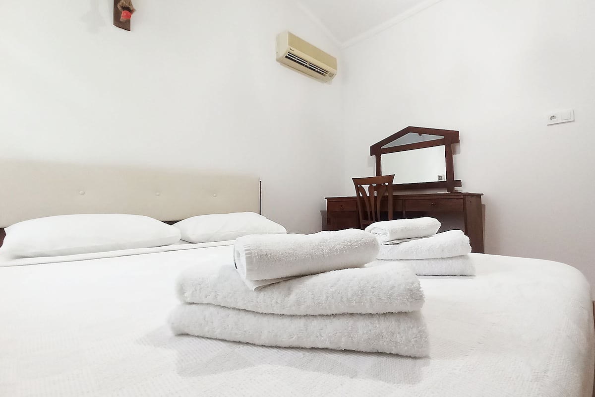 A neatly made bed with white towels, a wooden dresser with a mirror, and an air conditioning unit on the wall.