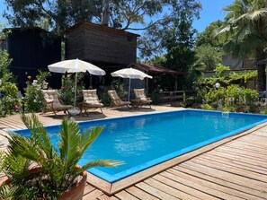 Une piscine rectangulaire avec une terrasse en bois, entourée de chaises longues et de parasols.