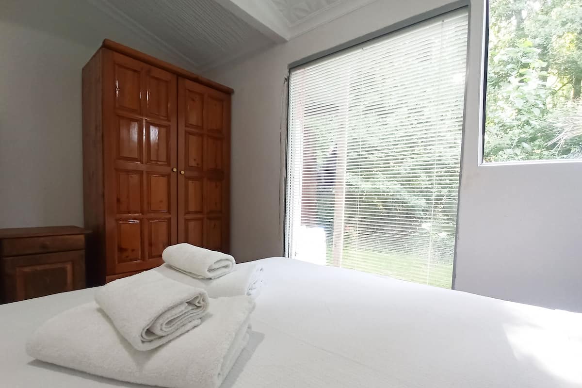 A bedroom with a large window, a wooden wardrobe, and two neatly folded white towels on the bed.