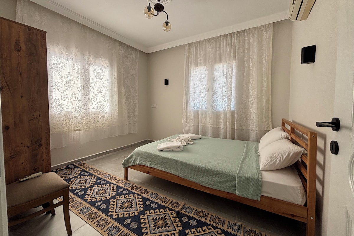 A bedroom with a bed, a wooden chair, a patterned rug, and a ceiling light fixture.