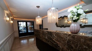 A marble reception desk with a vase of white flowers, a mirror, and two hanging crystal chandeliers in a hallway. - Suites Londres 212 (Mexico City)