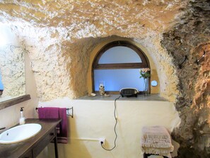 Un baño con pared de piedra, un lavabo blanco, una toalla morada y un ventanal con vistas.