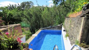 A rectangular swimming pool with a blue mosaic tile interior, surrounded by lush greenery and a stone wall. - Vivelorural: Alpendre de Ayala, piscina y jardín (Santa Brígida)