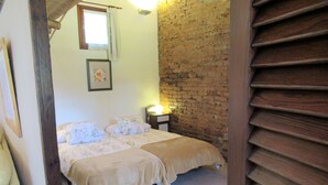 A bedroom with two beds, a brick wall, and a window with curtains. - Vivelorural: Alpendre de Ayala, piscina y jardín (Santa Brígida)