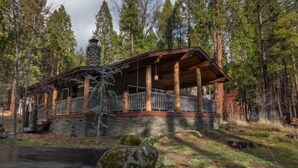 Une cabane avec des fondations en pierre, une terrasse en bois et une cheminée.