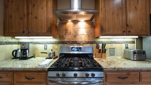 Une cuisine avec des meubles de rangement en bois, une cuisinière à gaz, une machine à café et un grille-pain.