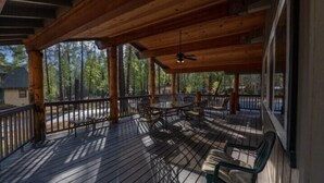 Une terrasse en bois, agréée d’une table et de chaises, entourée d’une rambarde et offrant une vue sur une zone boisée.