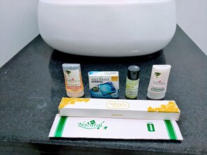 A bathroom counter with a white toilet, a shower gel bottle, a box of MEDIALAX clear glycerine, a bottle of Natural's herbal shampoo, a bottle of Natural's moisturizer, and a dental kit.