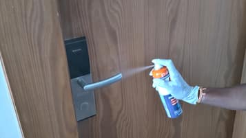A person using a spray bottle labeled "Ethanol" near a door handle.