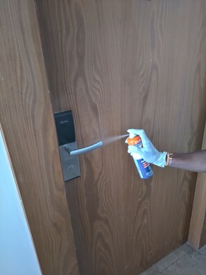 A person using a spray bottle labeled "Ethanol" near a door handle.