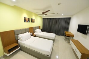 A hotel room with two beds, a desk, a TV, and a ceiling fan. - Hotel Sri Ram Grand (Vijayawada)