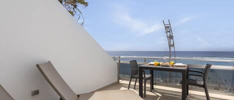 A balcony with a table set for breakfast, overlooking the ocean.