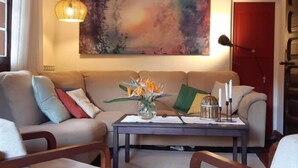 Una sala de estar con sofá, sillas, una mesa de centro, un cuadro y una lámpara colgante.