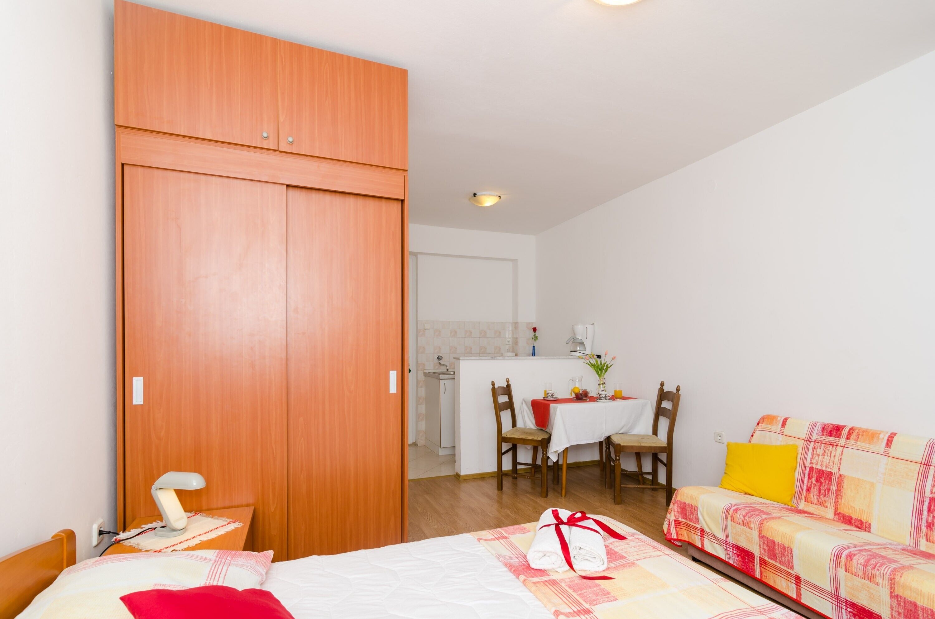 Une chambre à coucher comprenant un lit, une table de chevet avec une lampe, une armoire en bois, un coin repas avec une table et des chaises, et un canapé recouvert d’un tissu à motifs.