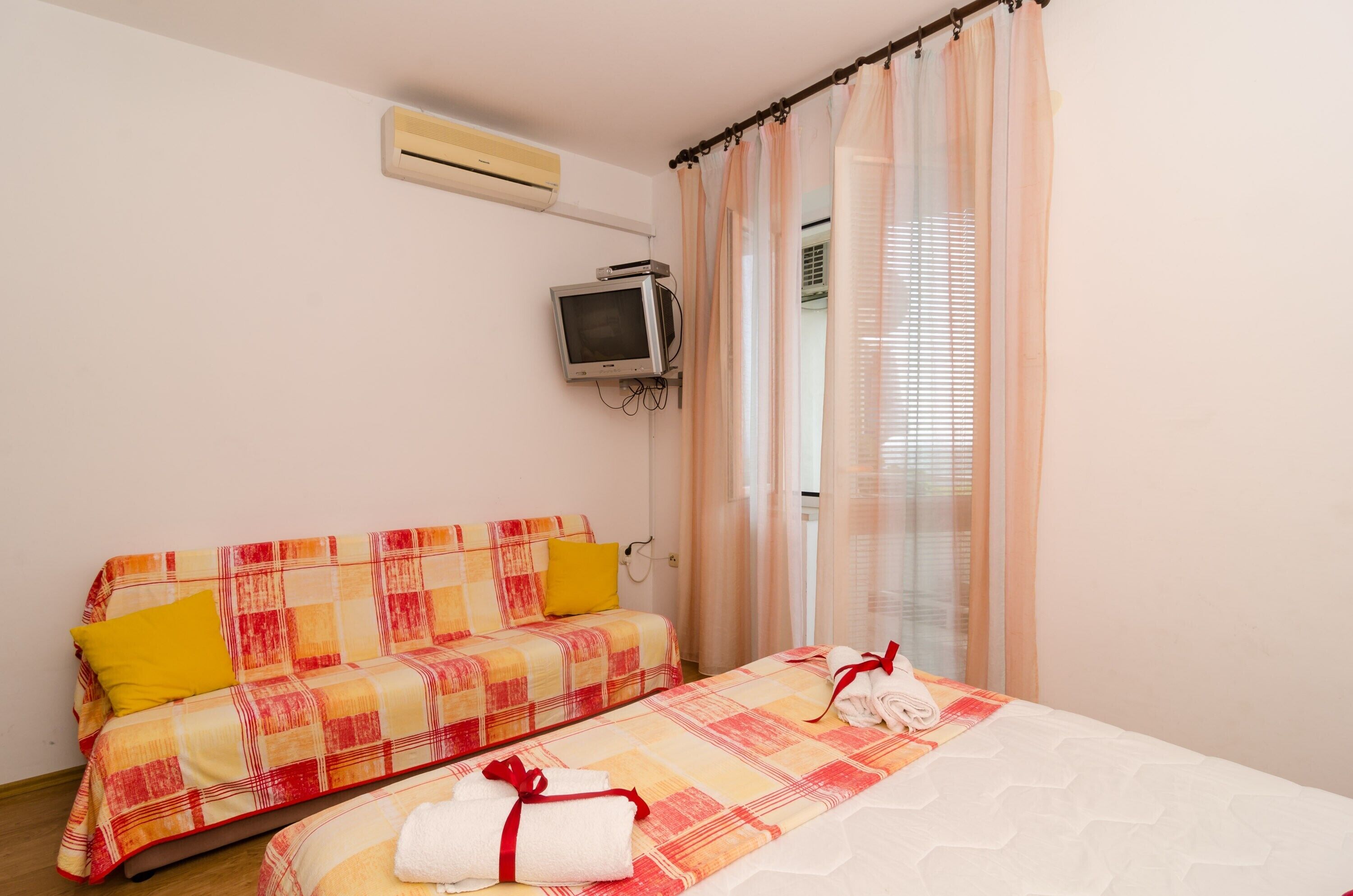 Ein Zimmer mit einem Bett, einem Schlafsofa, einem Fernseher und einem Fenster mit Vorhängen.