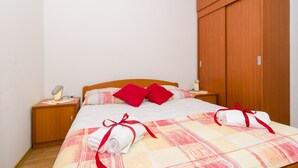 Un lit bien fait, agrémenté d’oreillers rouges, une armoire en bois et une lampe de chevet.