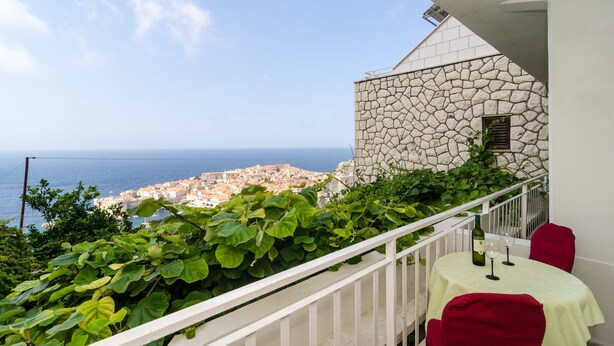 Un balcon avec un mur en pierre, une table recouverte d’une nappe et une bouteille de vin.