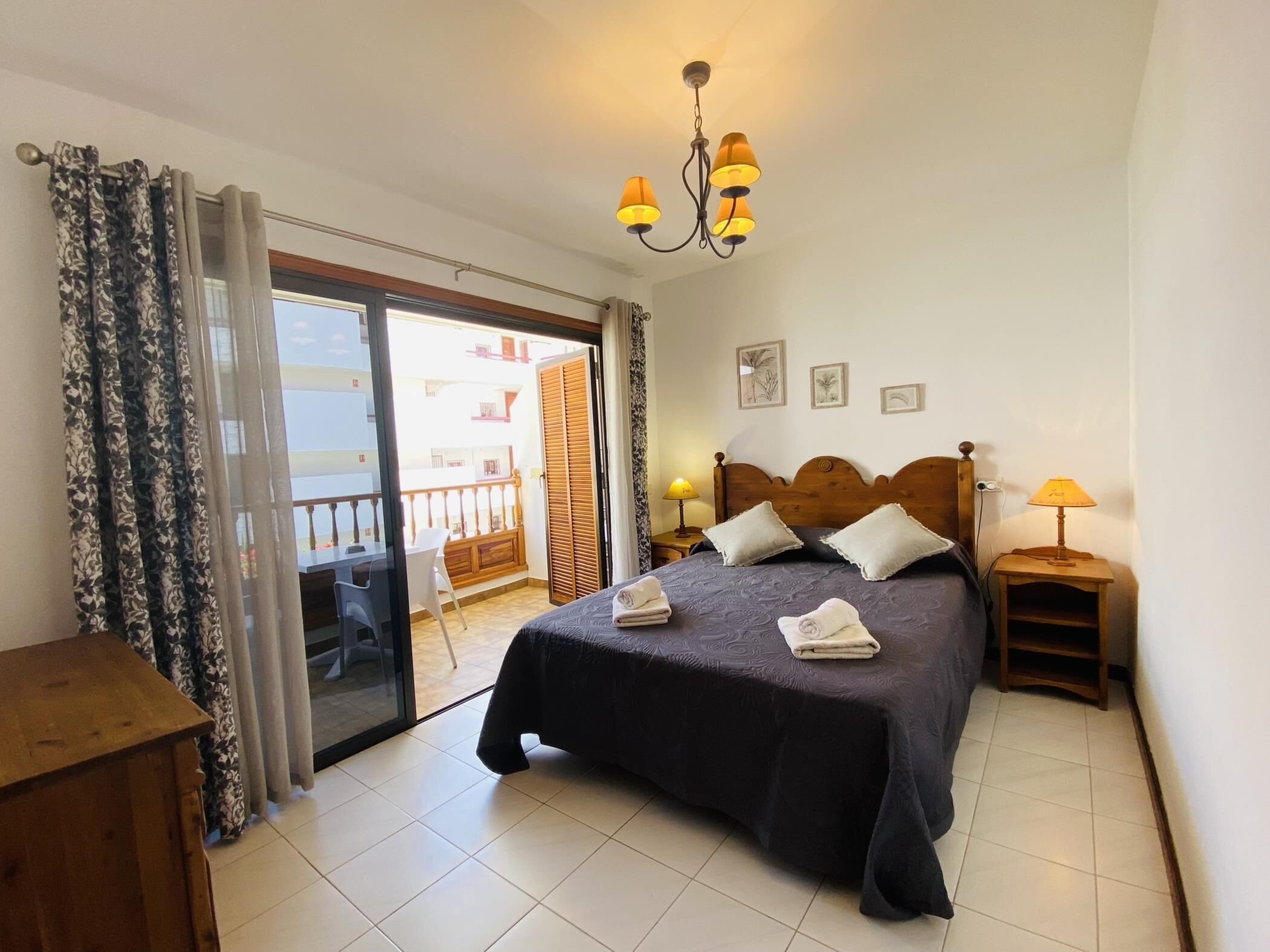A bedroom with a bed, two bedside lamps, a wooden headboard, a nightstand, a desk, and a chair.