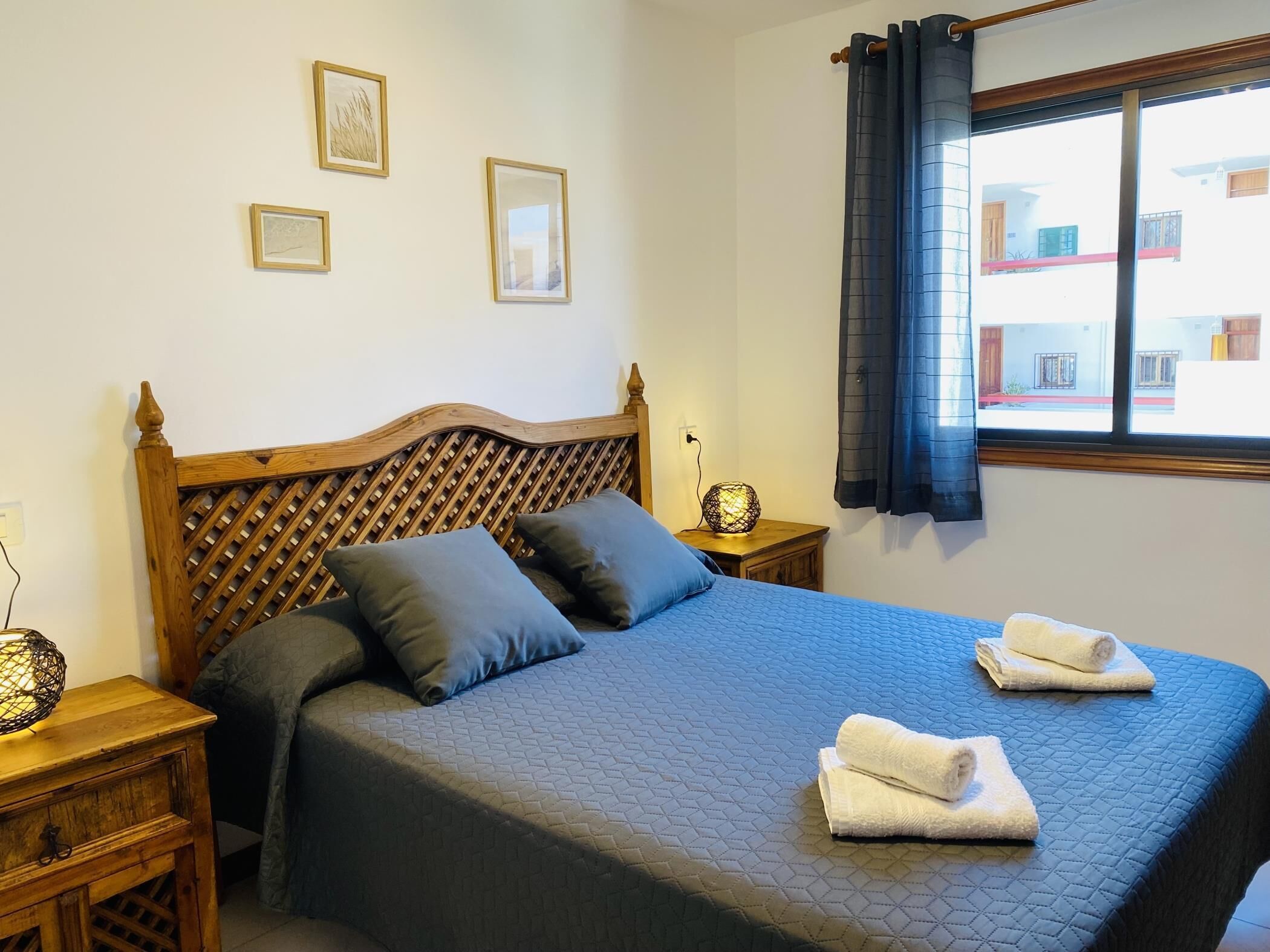 A neatly made bed with a quilted blue bedspread, two pillows, and two folded towels on the side.