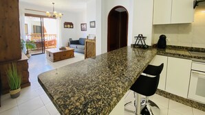 Eine moderne Küche mit Granit Arbeitsplatten, weißen Schränken und einem Essbereich mit einer Couch und Couchtisch.