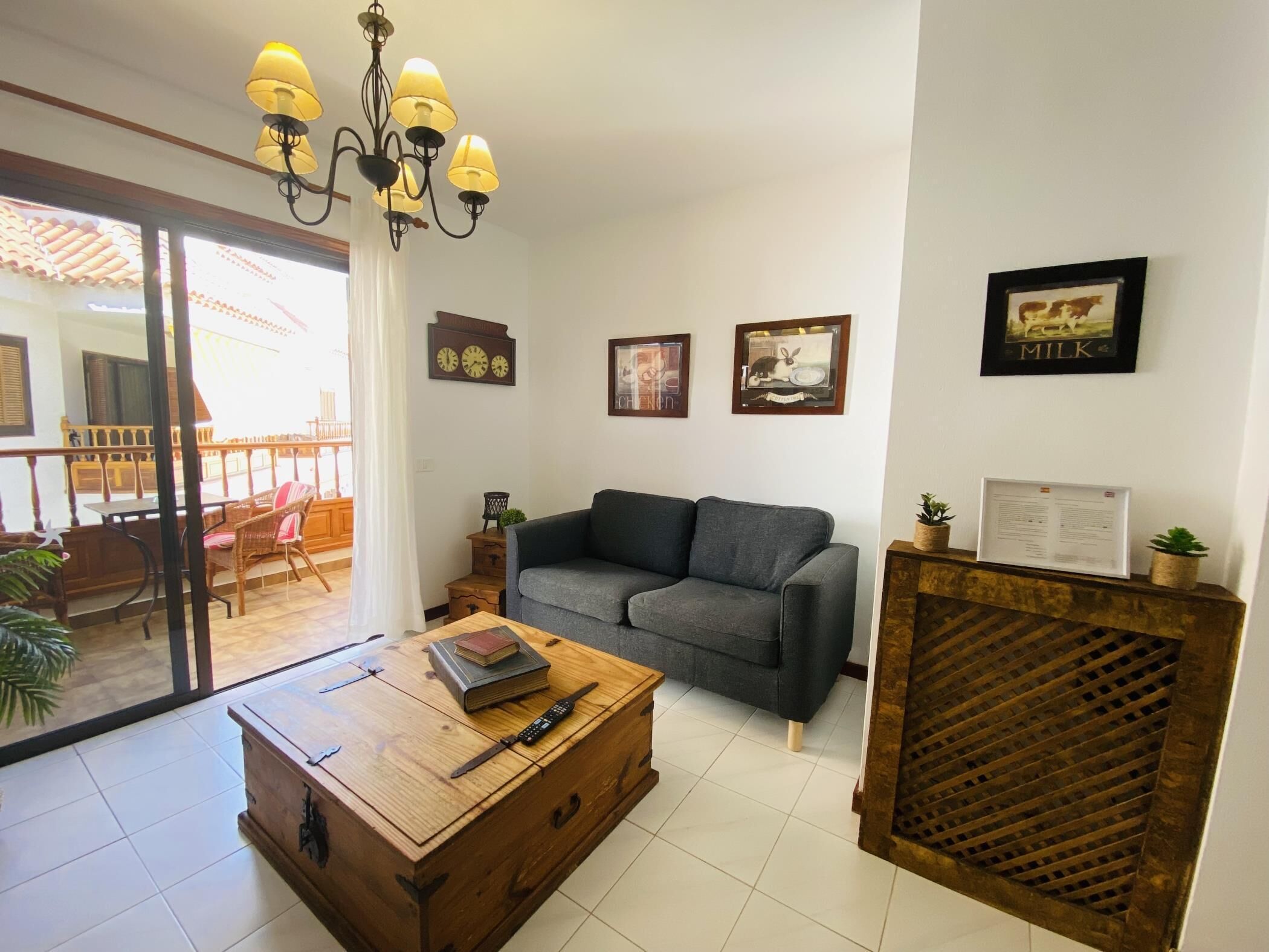 Una sala de estar con sofá, mesa de centro de madera, candelabro y vistas a un balcón exterior.