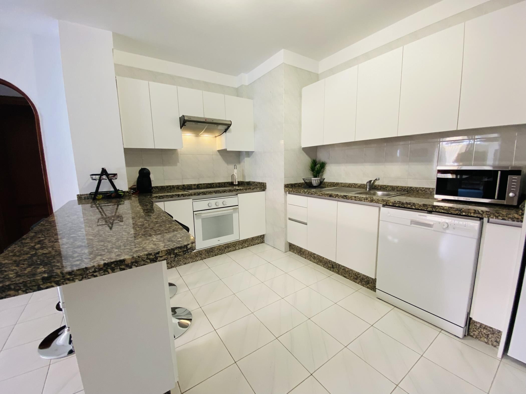 A modern kitchen with white cabinets, granite countertops, a built-in oven, a microwave, and a dishwasher.