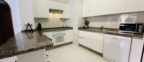 A modern kitchen with white cabinets, granite countertops, a built-in oven, a microwave, and a dishwasher.