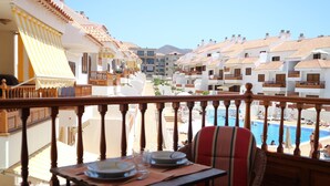 Ein Balkon mit Esstisch, der auf einen Pool und eine Reihe von Gebäuden mit Terrakotta-Dächern blickt.