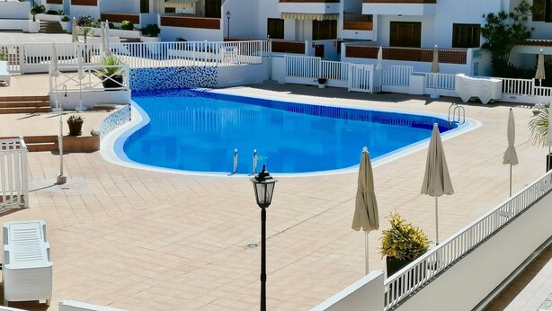 Ein Swimmingpool, umgeben von weißen Gebäuden mit Balkonen, einer gefliesten Terrasse und Gartenmöbeln.