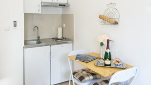 A compact kitchen with white cabinets, a stainless steel sink, and a small dining table with a chair. A decorative wire basket hangs on the wall above the table. - Studios IM - Studio Apartment with Shared Terrace (A1) (Dubrovnik)