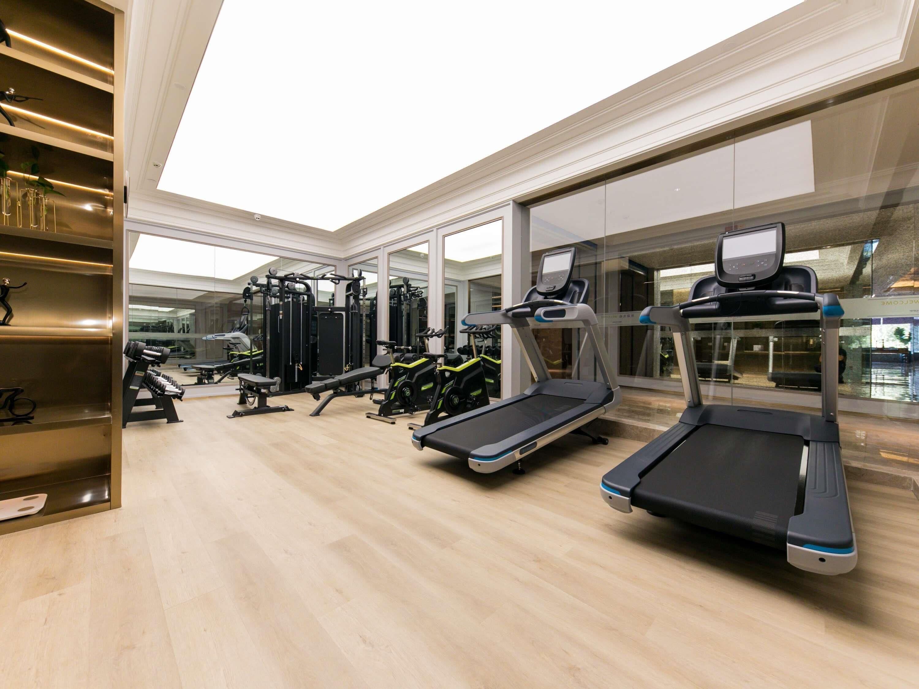 A modern gym with treadmills, weight machines, and a mirrored wall.