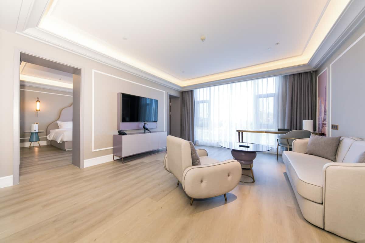 Quarto de hotel moderno com televisão de tela plana, sofá, mesa de jantar e cama.