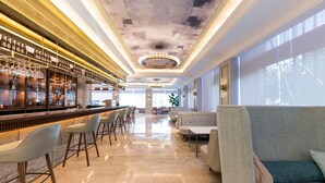 A bar area with a long counter, bar stools, and a seating area with sofas and tables. - Mercure Turpan Downtown (Turpan)