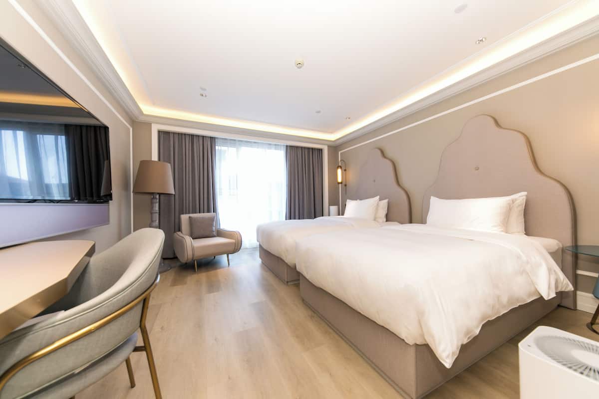 Quarto de hotel moderno com uma cama grande, uma escrivaninha, uma cadeira e uma mesa de cabeceira.