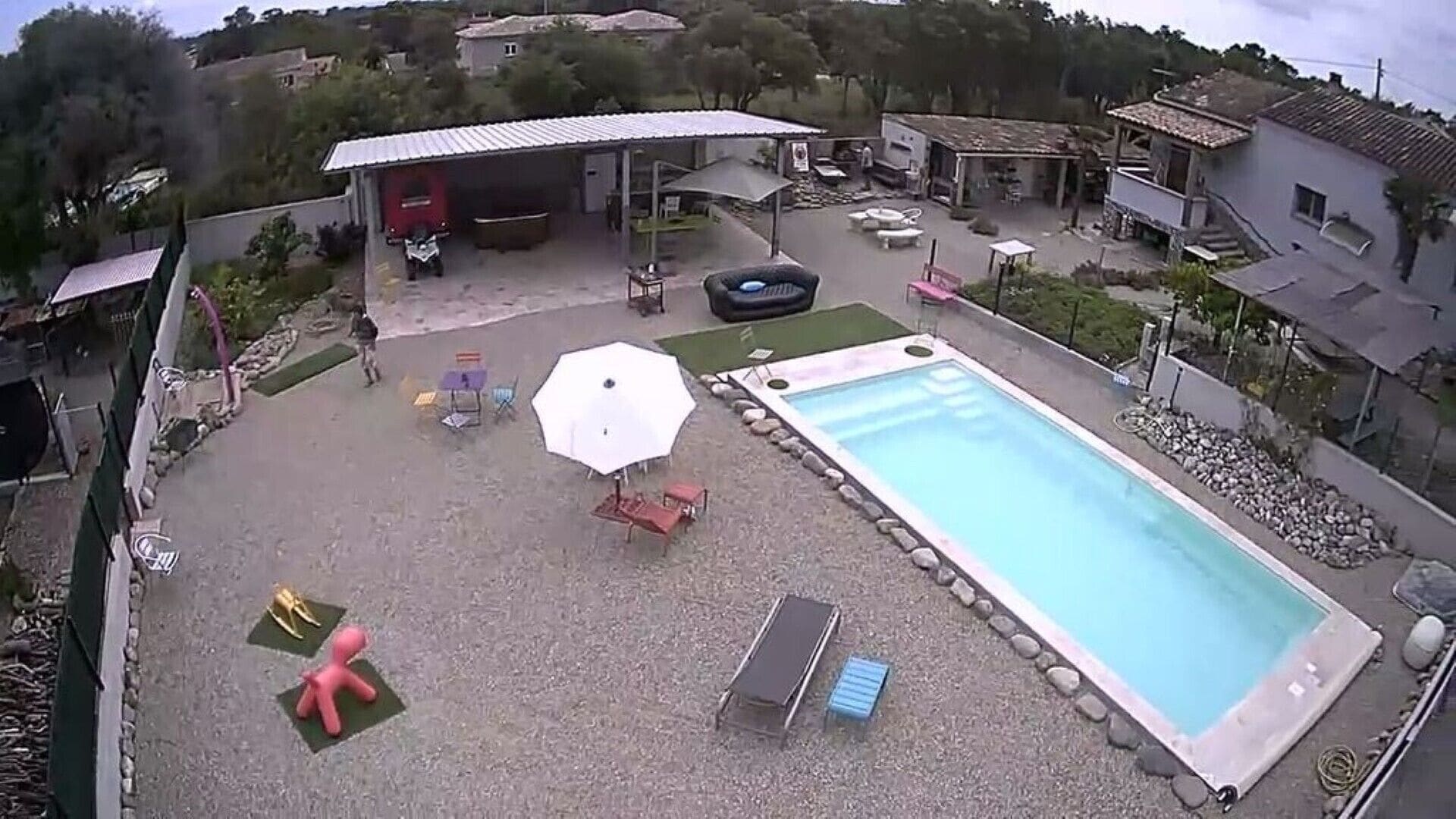 Ein Außenpool mit einer Terrassenfläche, einem überdachten Sitzbereich und einem kleinen Geräteschuppen.