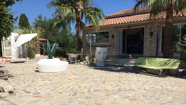 Une terrasse dallée de pierres, agrémentée d’un jardinière blanche, d’un banc et d’un bâtiment doté d’un toit en tuiles.