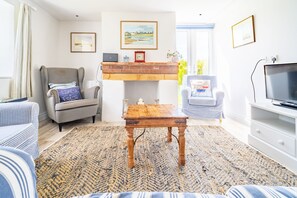 Una sala de estar con chimenea, un sofá, una silla, un televisor y una alfombra.