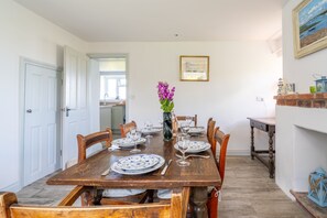 Comedor con mesa de madera dispuesta para seis personas, rodeado de sillas y un jarrón con flores sobre la mesa.