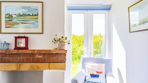 Une pièce avec une cheminée, un fauteuil, une horloge et une fenêtre donnant sur un paysage verdoyant.