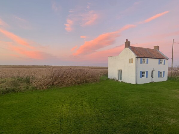Una casa blanca con contraventanas azules, techo rojo y un pequeño jardín delantero.