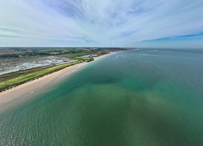 Une vue aérienne d’une zone côtière avec une plage, des champs verdoyants et un ciel dégagé.