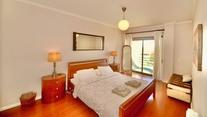 Une chambre à coucher avec un lit, des tables de chevet, un miroir, une lampe et une vue sur l’extérieur.