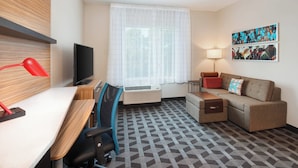 A hotel room with a desk, chair, sofa, TV, air conditioning unit, lamp, and artwork on the wall. - TownePlace Suites by Marriott Atlanta Lawrenceville (Lawrenceville)
