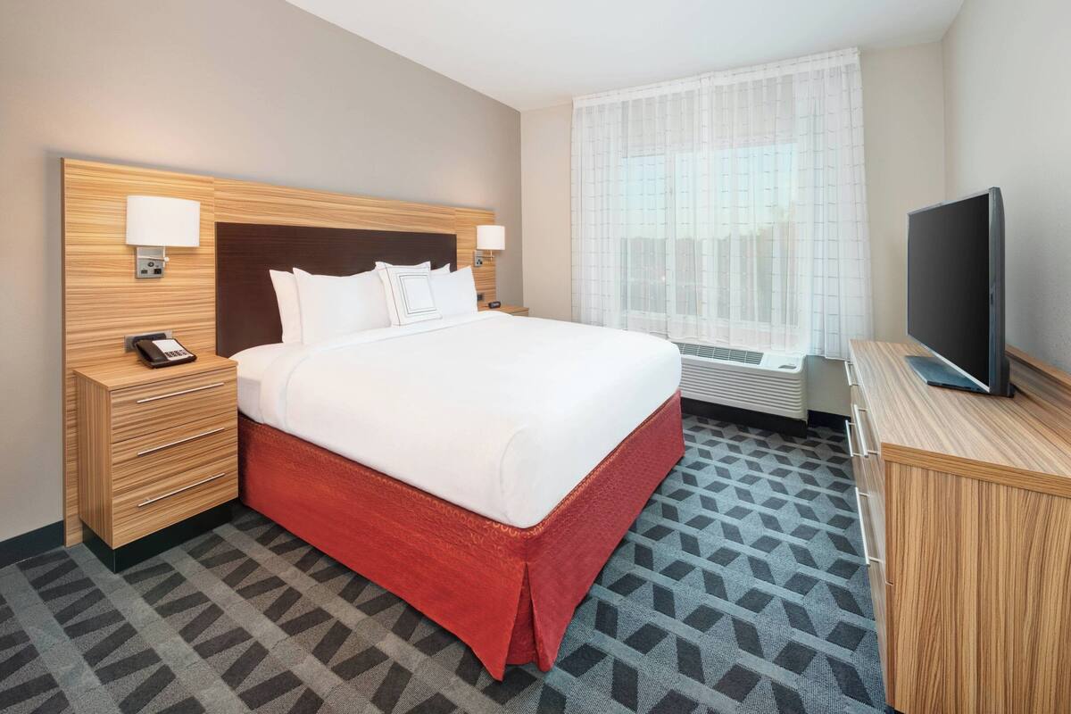 Une chambre d’hôtel avec un grand lit, des tables de chevet, une télévision et une fenêtre avec des rideaux.