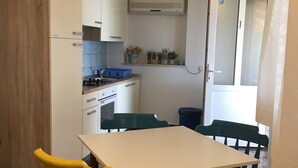 Una cocina compacta con armarios blancos, una estufa y un lavabo. Hay dos sillas amarillas y una mesa en el comedor.