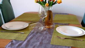 A dining table set with two plates, two wine glasses, a bottle of wine, and a vase with yellow tulips. - Apartments Cumbelic - One Bedroom Apartment with Balcony and Sea View A3 (Kozarica)