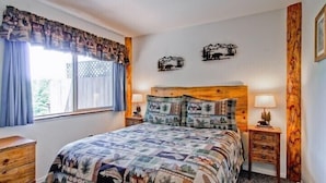 A bedroom with a large bed, two nightstands, a window with curtains, and two wall decorations. - Scenic Wonders Alpine View 2 Bedroom (Yosemite National Park)