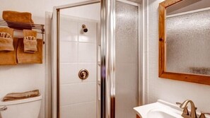 Un baño con ducha, inodoro y lavamanos. Hay toallas colgadas en un perchero.