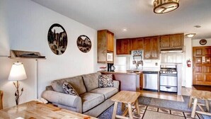 A living room with a sofa, coffee table, and lamp. There is a kitchen with wooden cabinets and a stove. - Scenic Wonders Alpine View 2 Bedroom (Yosemite National Park)